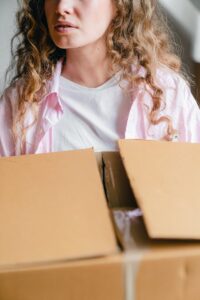 Crop serious young lady carrying carton box at home