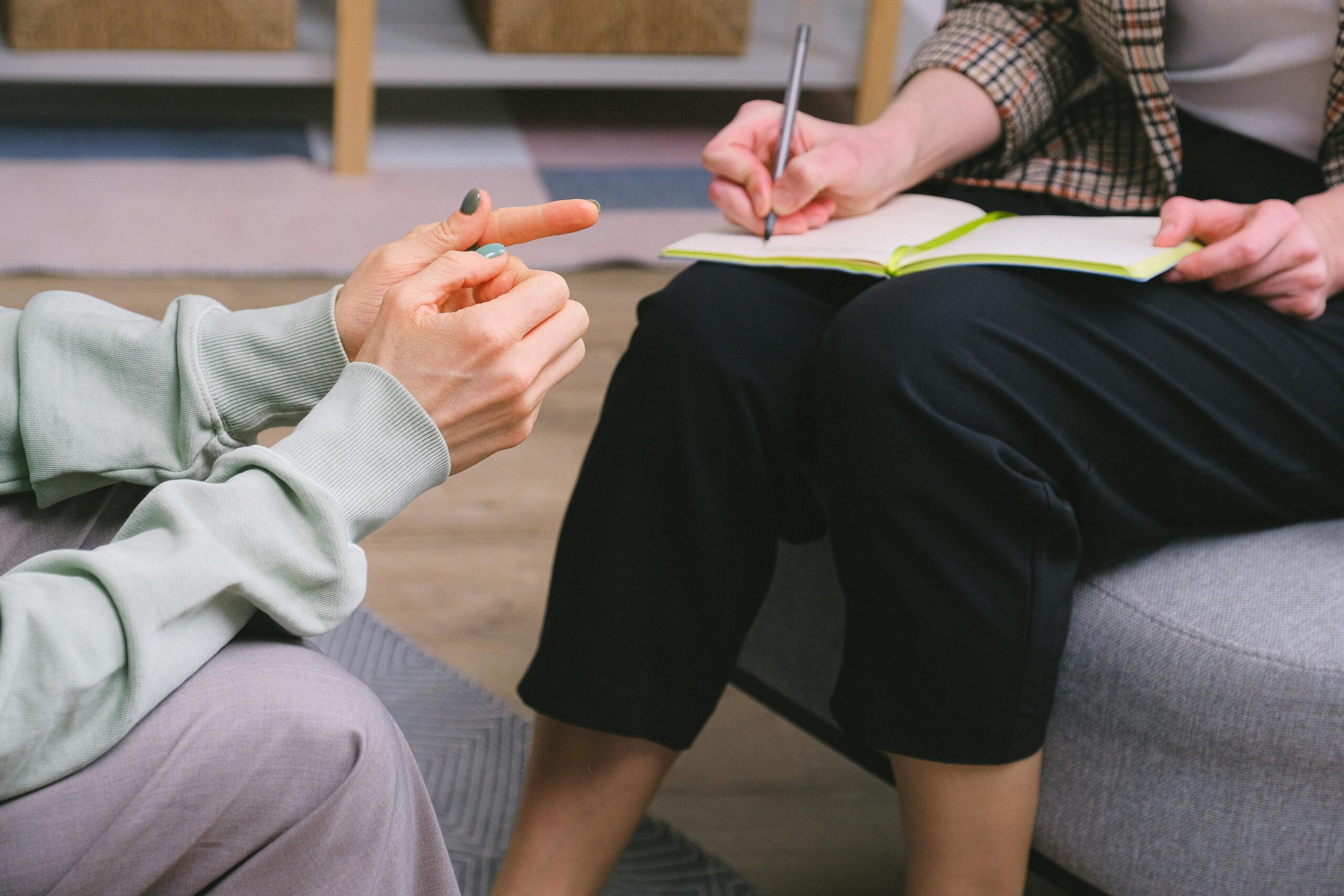 Close-up of a Psychiatric session showing a patient gesturing with their hands while the therapist takes notes in a notebook
