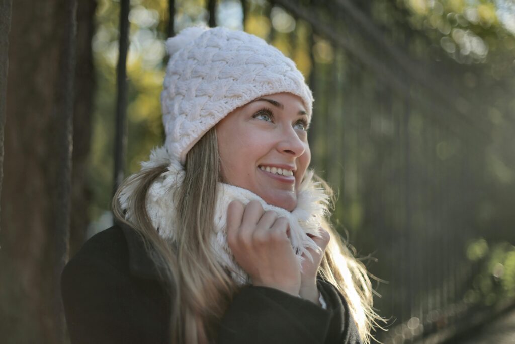 A woman standing outside smiling while holding her scarf wrapped around her neck.